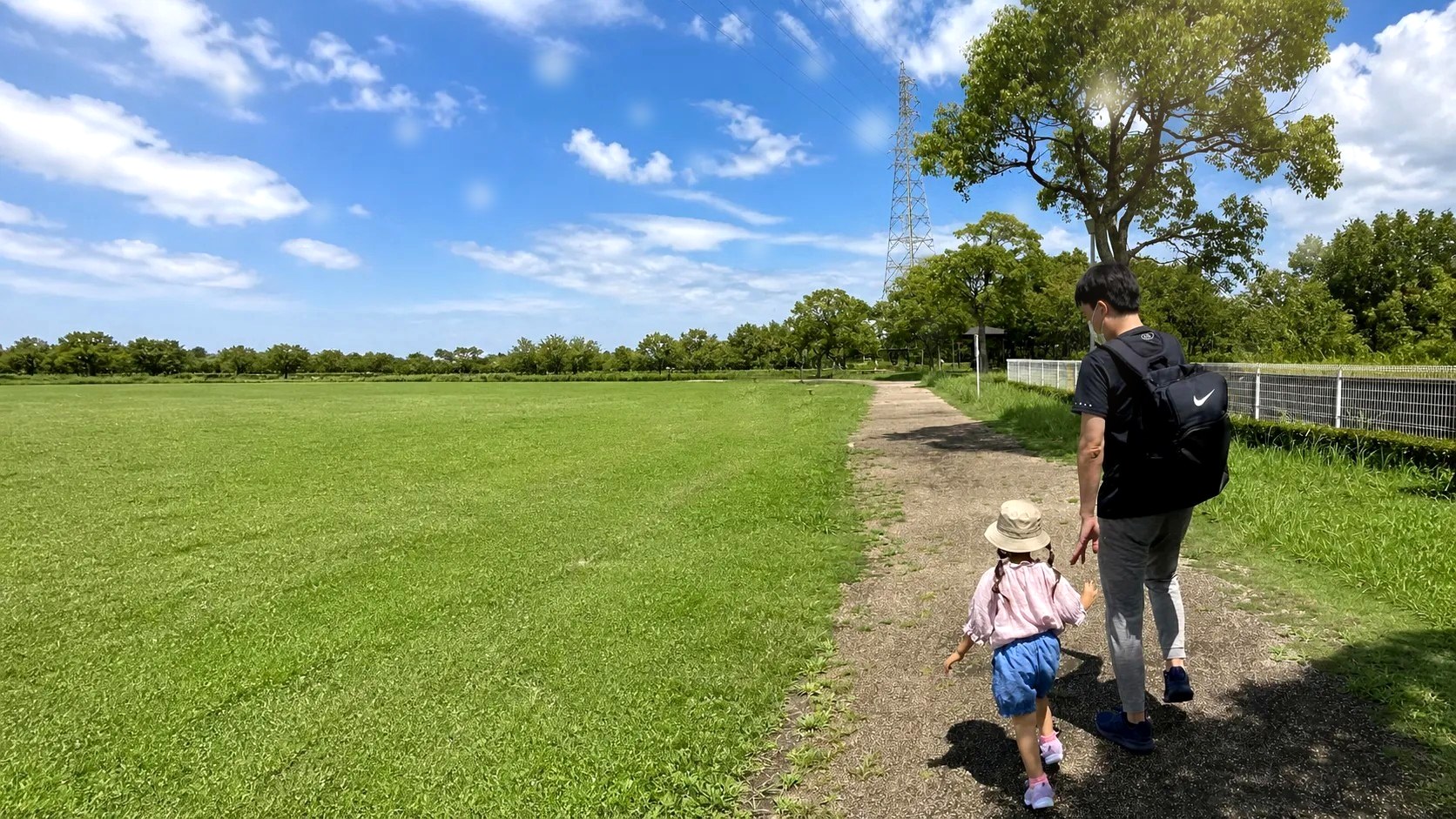 青空の公園の道を歩く父と娘のうしろ姿