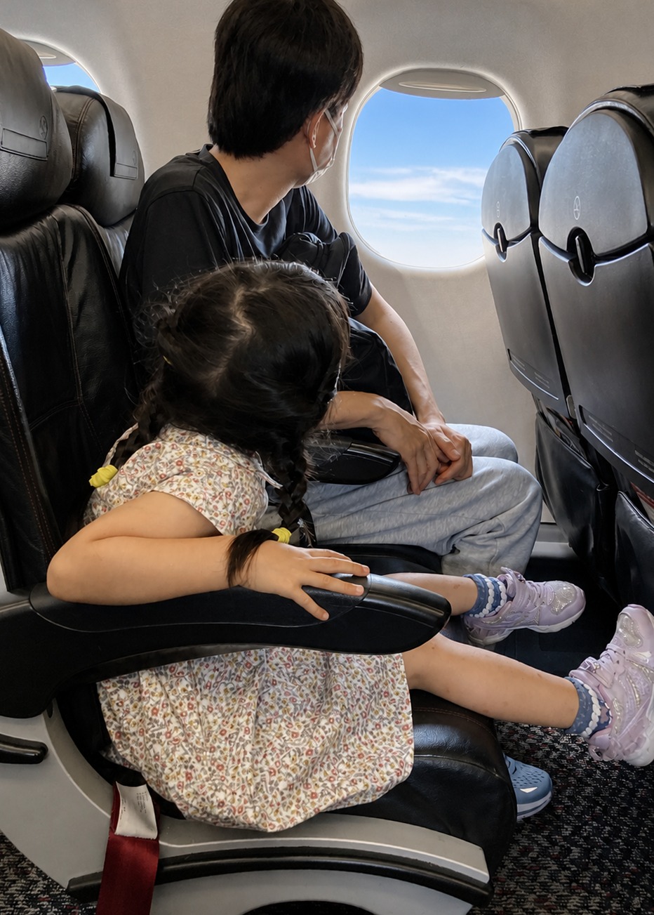 飛行機の座席から窓の外を見る父と娘